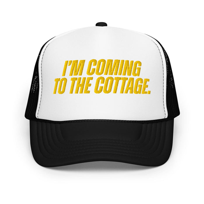 A black and white trucker hat with yellow text on the front panel reading 'I'M COMING TO THE COTTAGE.' on a plain white background.